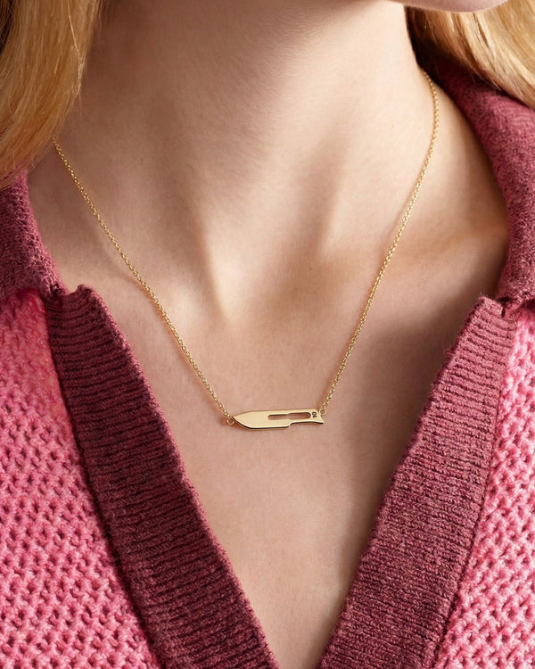 Model styling a gold necklace with a 10 Blade pendant with a collared pink polo top