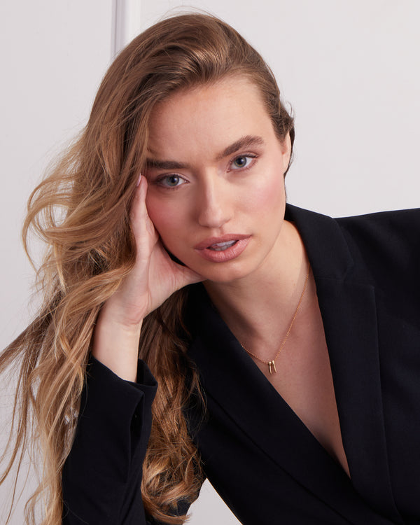 Woman wearing a gold necklace with tooth charms spelling 2025, styled with a black blazer on a white background