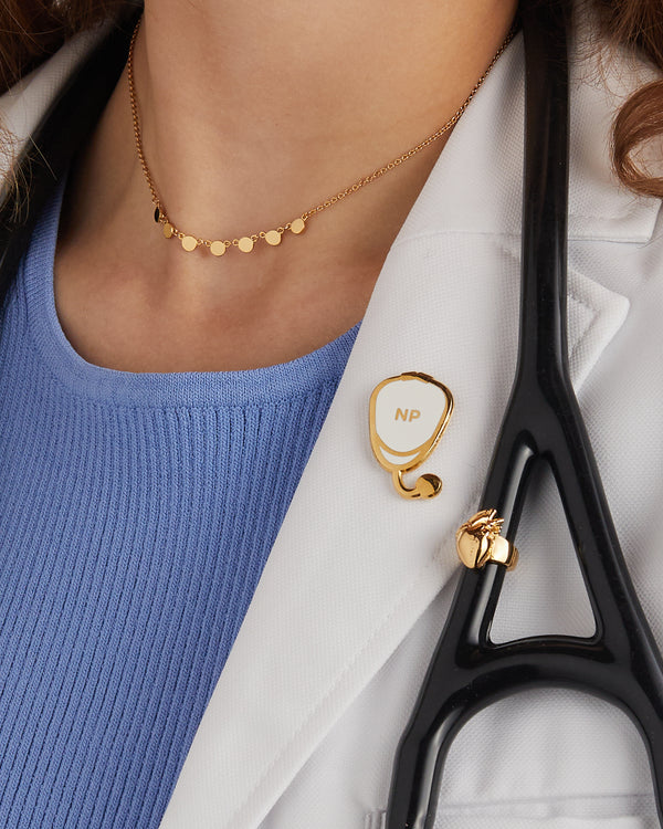 Gold plated stethoscope charm attached to black stethoscope tubing, worn with a white coat and gold necklace.