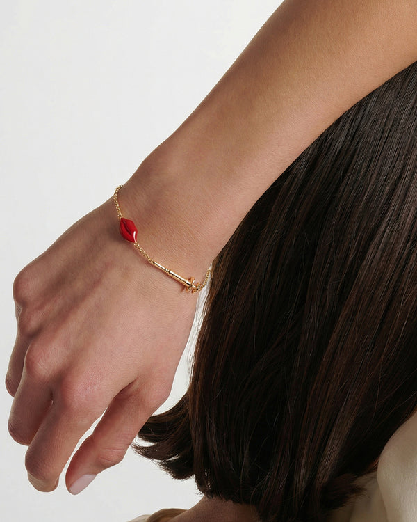 Gold bracelet with a red enameled lips charm and filler syringe charm modeled on a wrist