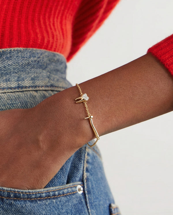 Gold bracelet with tooth and dental drill charms styled on a model wearing a red sweater and blue jeans